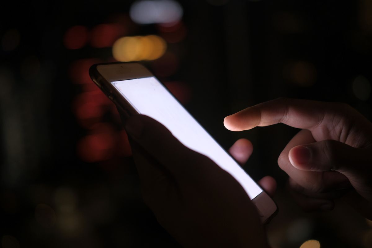 暗い夜に白く光るスマホを操作する手元