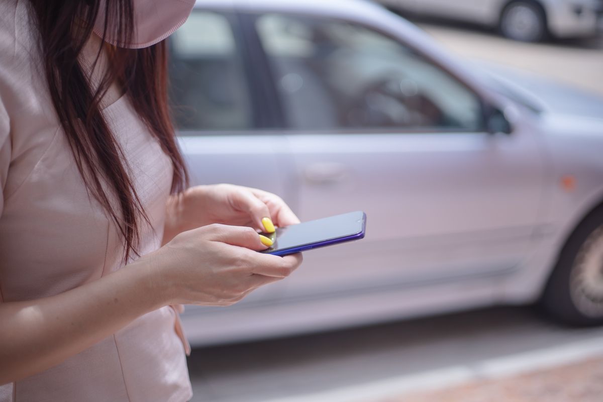 車の前でスマートフォンを操作する女性の手元