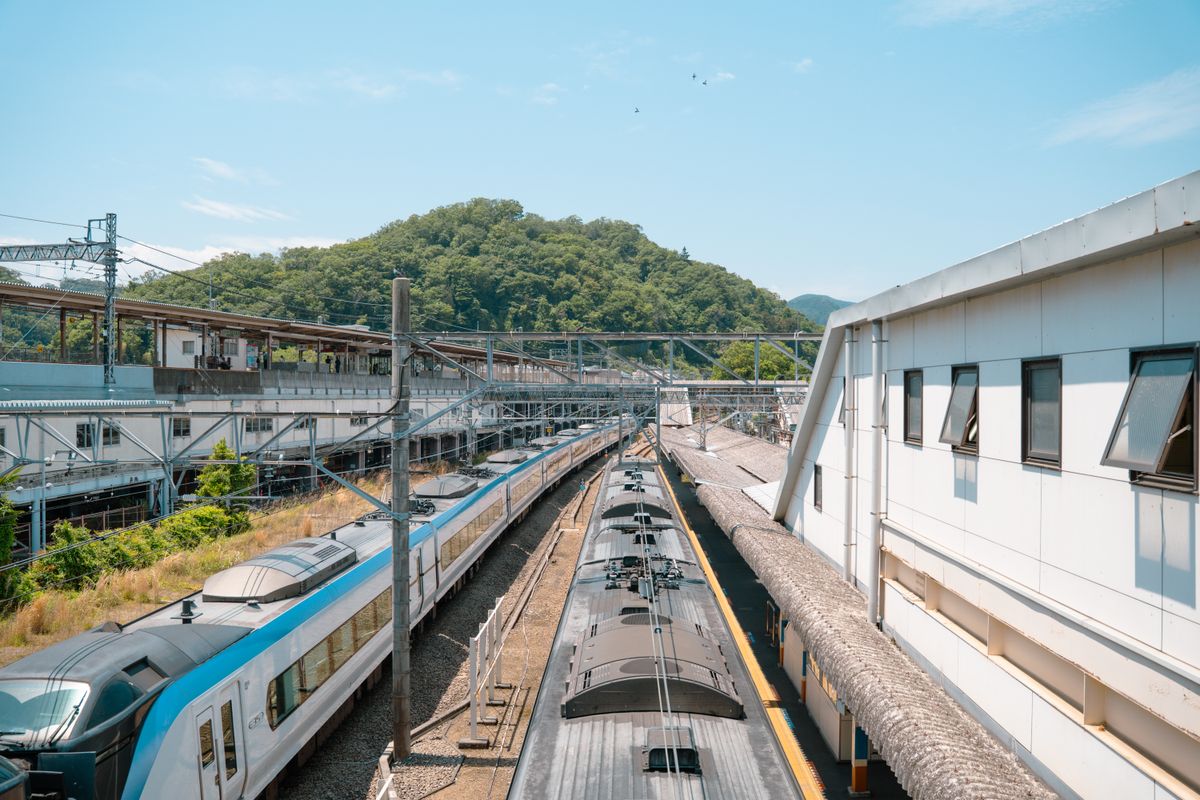 晴れた空の下、山を背にした駅の線路と電車